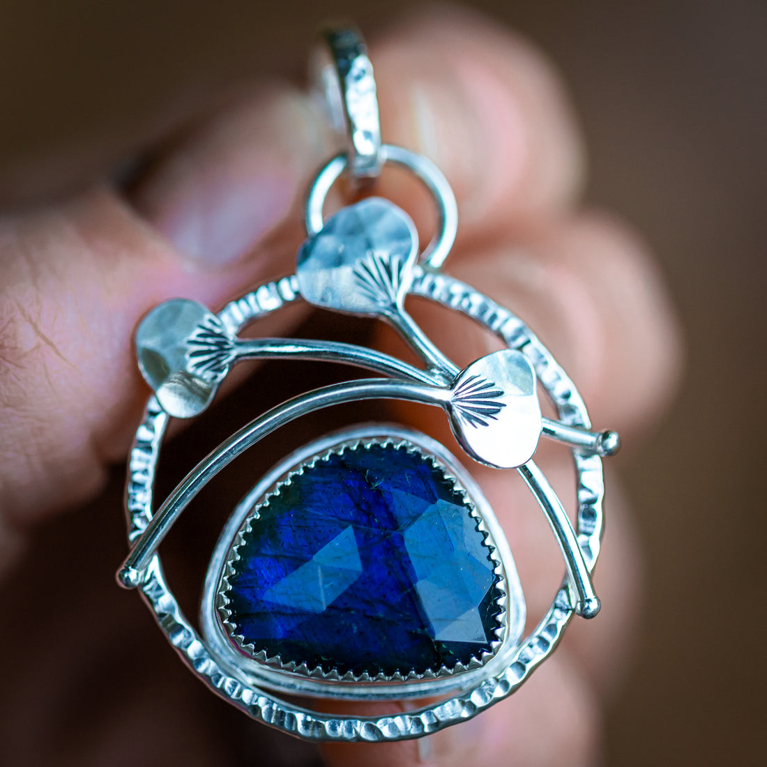 This unique handmade labradorite pendant has a gorgeous blue flash across the faceted surface.  Bezel set in solid sterling silver with hand sculpted botanical elements, this unique handcrafted pendant is one of a kind!